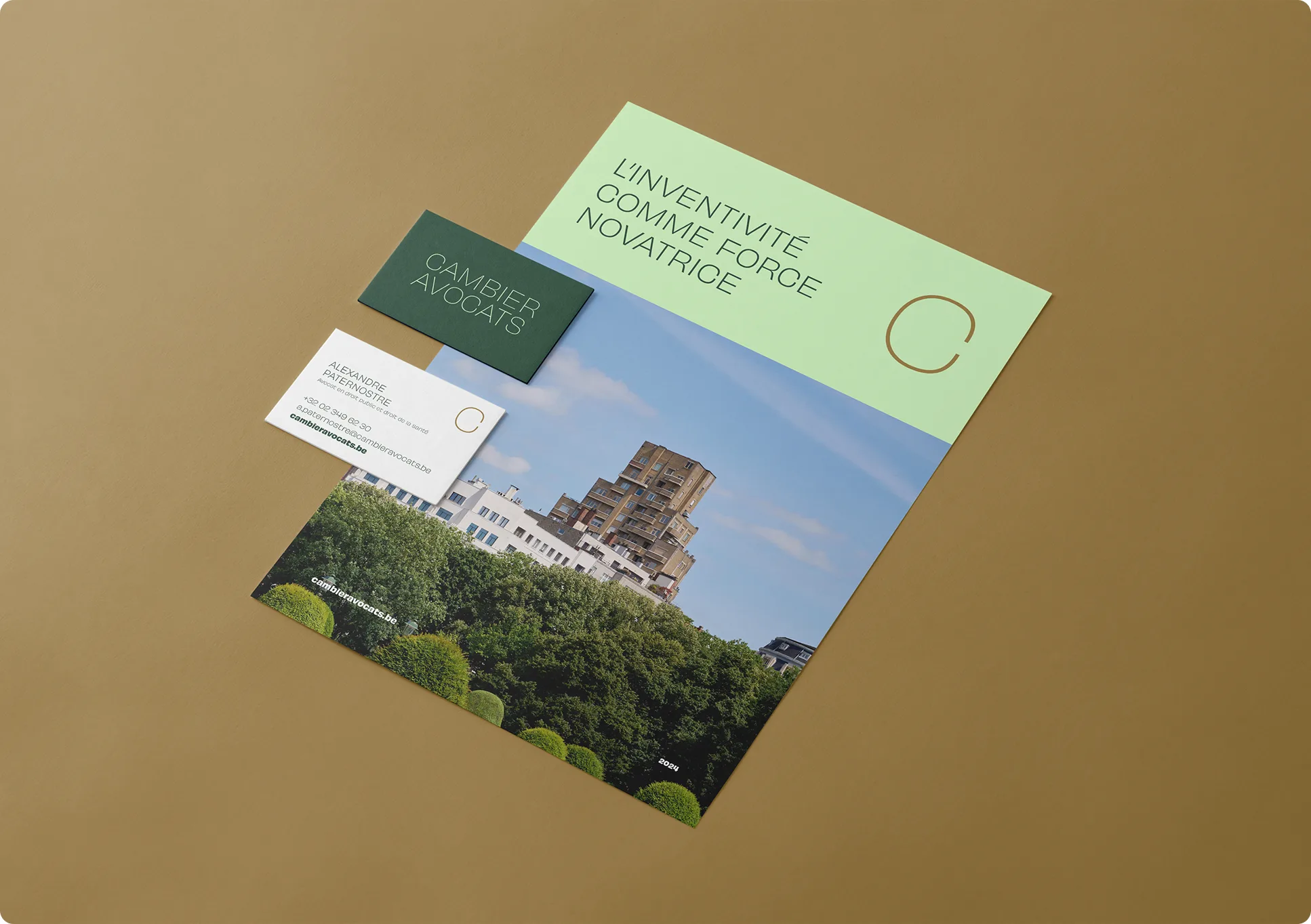 Ensemble d'articles de papeterie sur un support brun, comprenant une brochure avec une photo de paysage urbain et le texte L'inventivité comme force novatrice, une carte verte étiquetée Cambier Avocats et une carte de visite blanche.